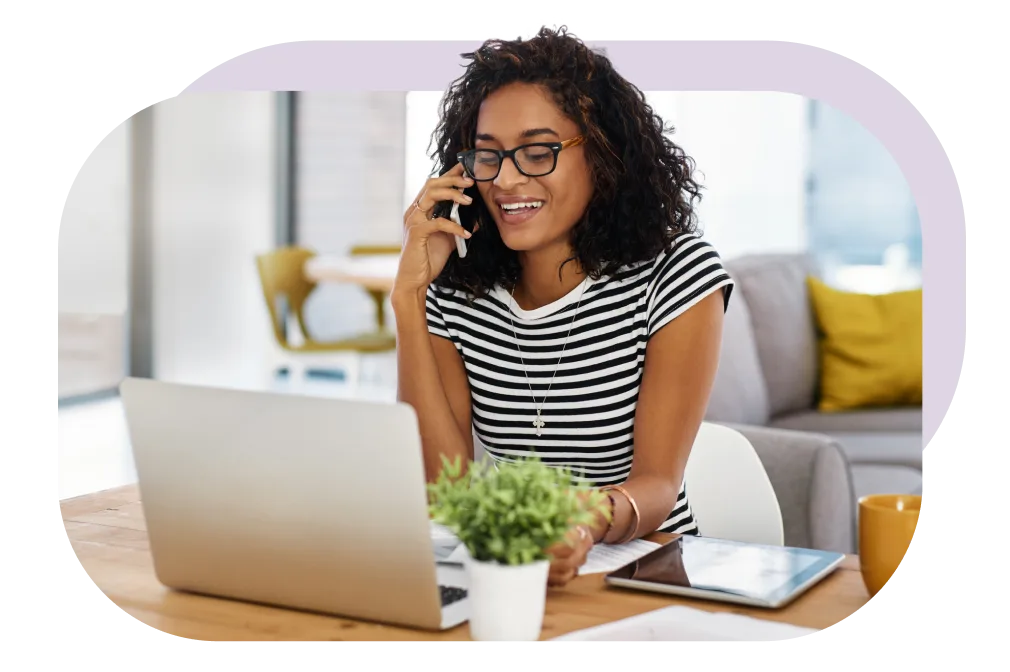 Woman is seated, talking on the phone in front of an open laptop 