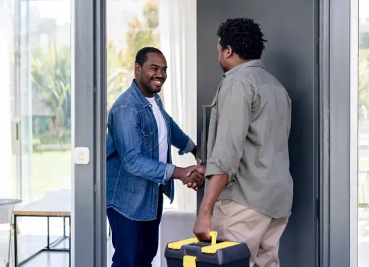 Un électricien certifié TELUS arrive à la maison pour installer et installer l’équipement Énergie intelligente, tandis qu’un homme l’accueille à la porte.