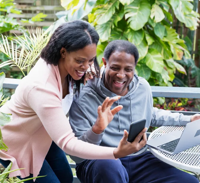 Un homme et une femme qui agitent la main et sourient font un appel vidéo sur leur smartphone.