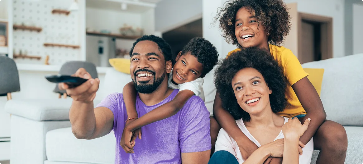 Family of four enjoying entertainment together as father uses remote control.
