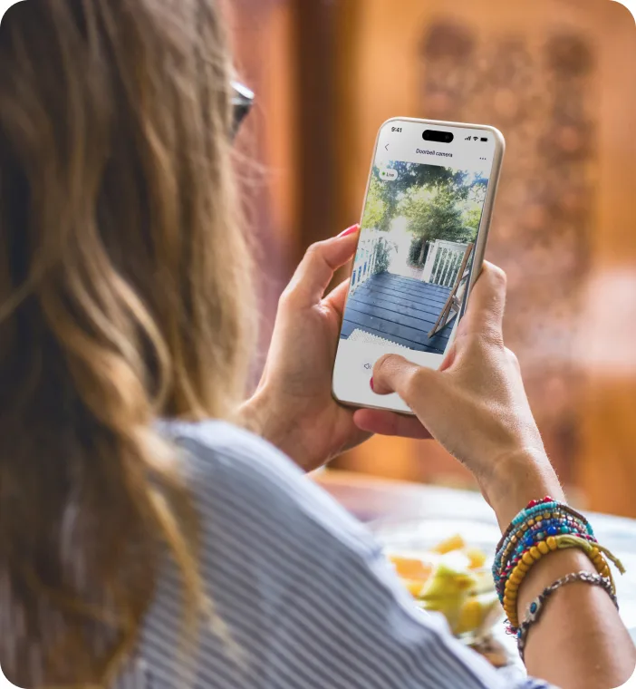 Femme examinant sur l’application TELUS MC+ les images issues d’une sonnette vidéo TELUS pendant sa pause repas à domicile. 