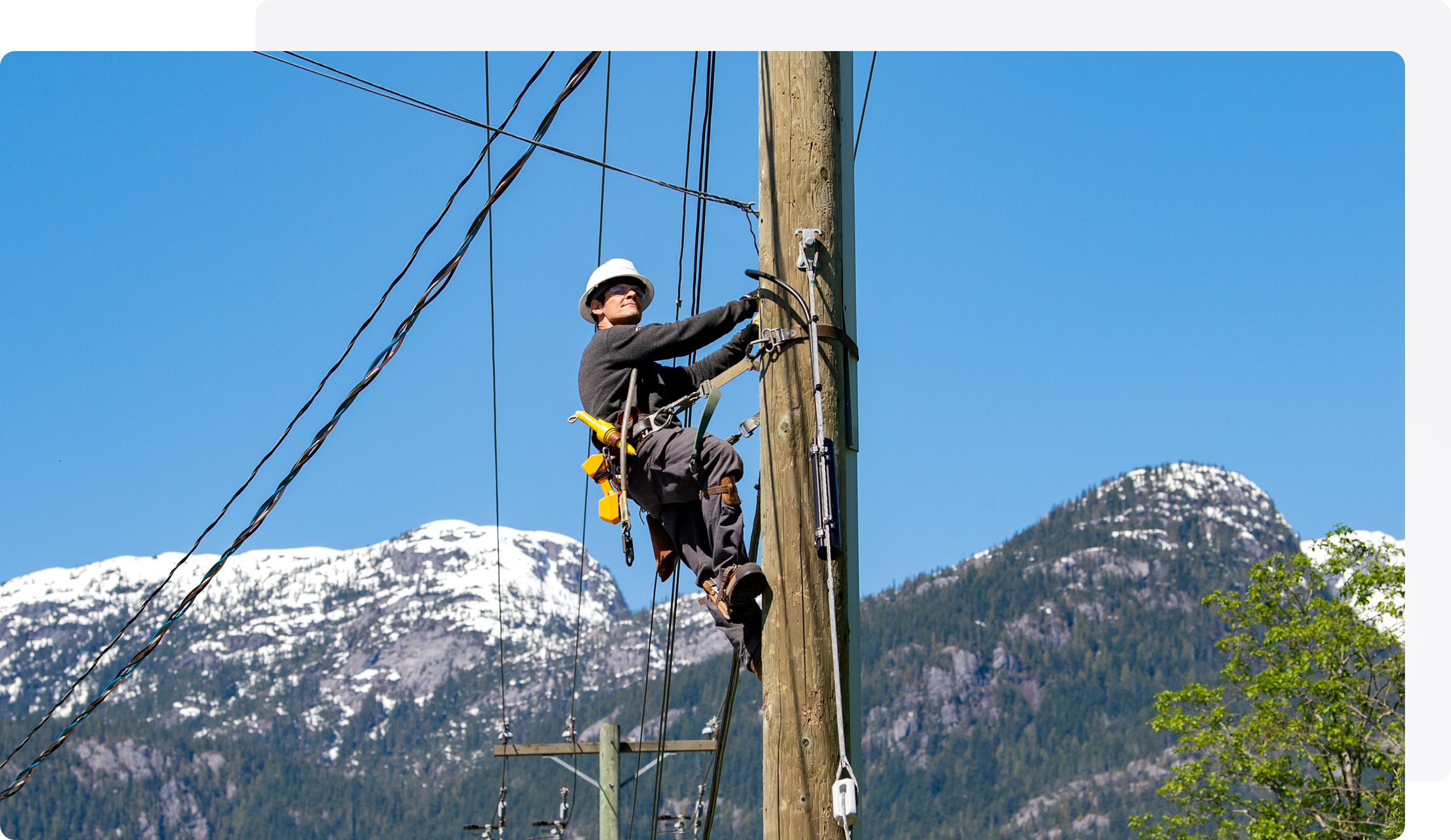 Ouvrier escaladant un poteau électrique devant des montagnes en arrière-plan