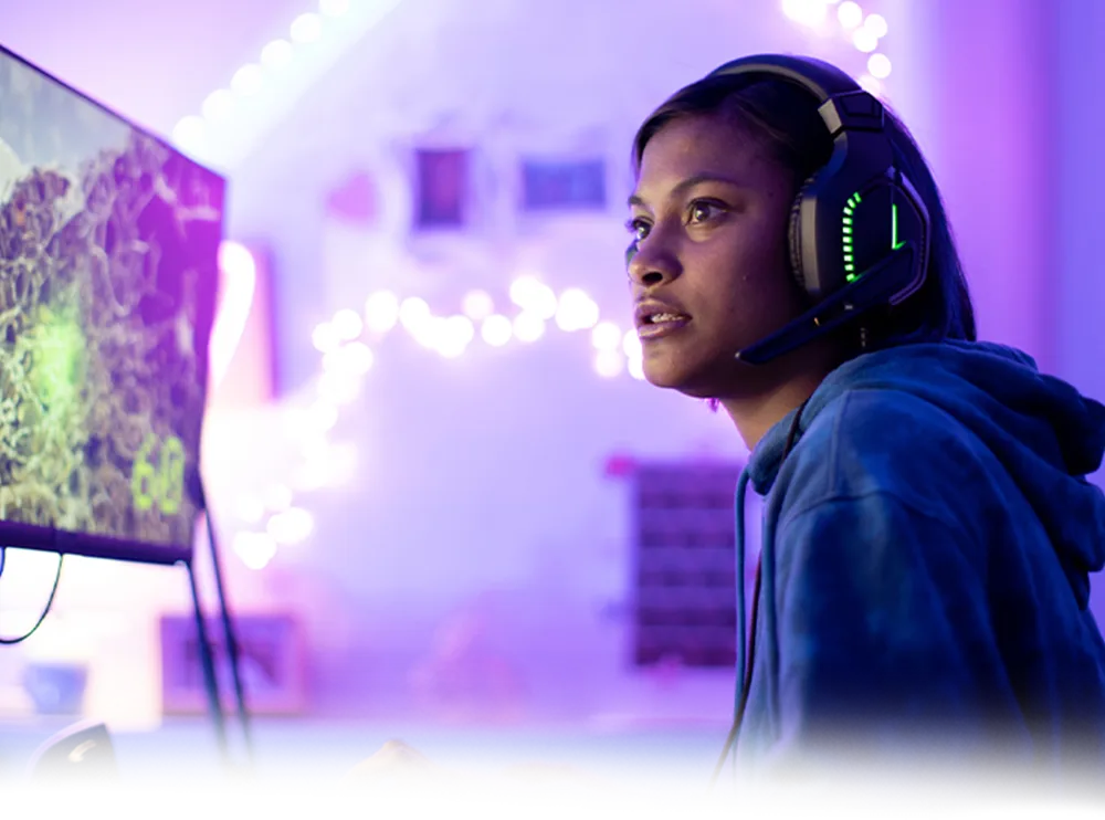 A woman stares intently at a screen as she wears headphones and plays a game.