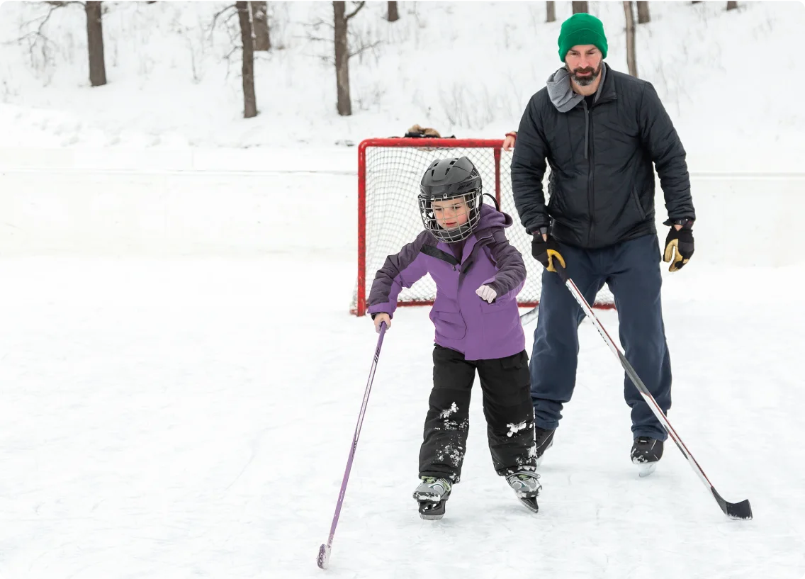 A child and adult skating on an outdoor rink.