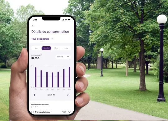 Une main tient un téléphone intelligent affichant l’interface de l’application Énergie intelligente, montrant des appareils intelligents et des routines manuelles sur un fond de parc ensoleillé.