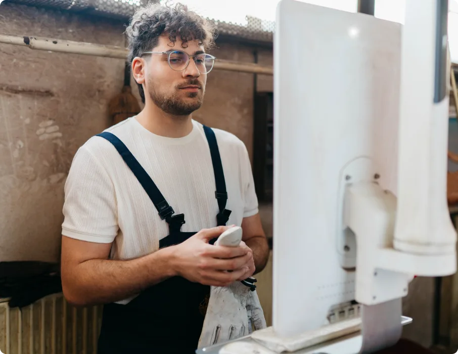 A shop worker uses a desktop computer at a workshop bench.