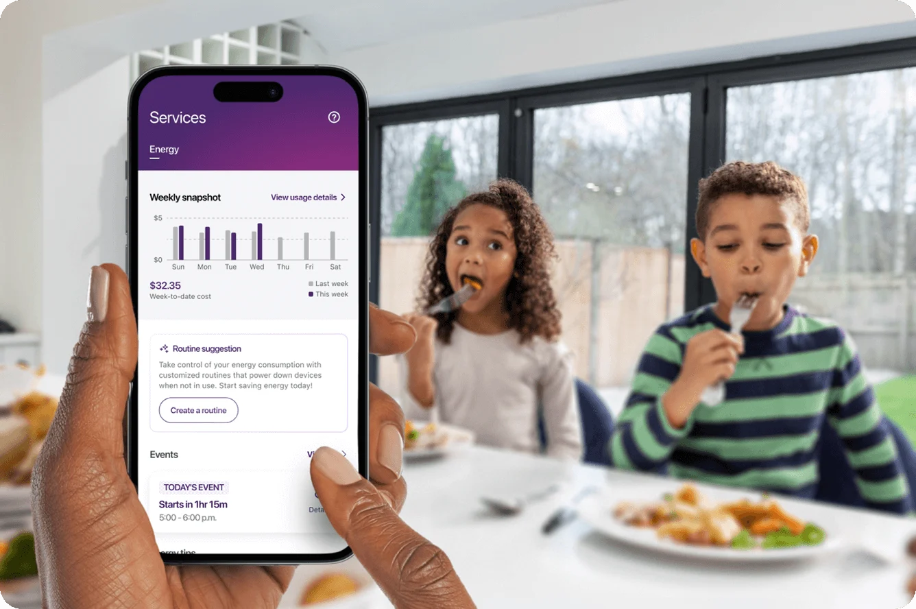 Hand holding smartphone showing energy consumption charts with family in background
