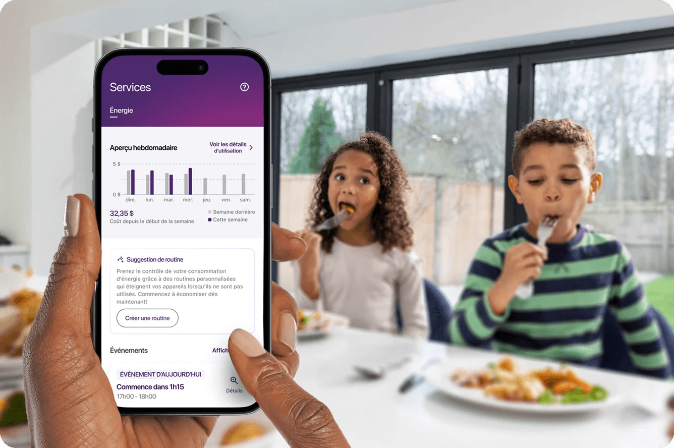 Une main tient un téléphone intelligent qui affiche les graphiques de consommation d’énergie, avec sa famille en arrière-plan
