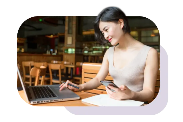 Femme travaillant sur un ordinateur portable avec appareil mobile en main.