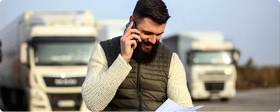 Truck driver on phone managing logistics with commercial vehicles in background.