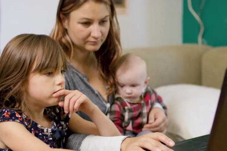 A mother and her two young children looking down at a laptop, symbolizing our Internet for Good program.