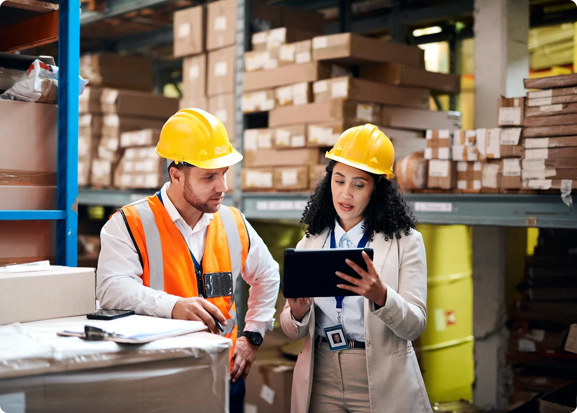 Warehouse supervisors reviewing inventory data on tablet in distribution center.