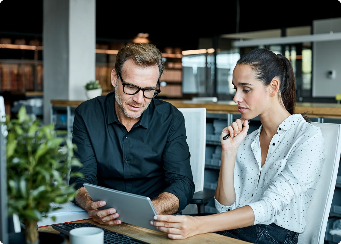 Two business professionals reviewing information on a tablet in a modern office.