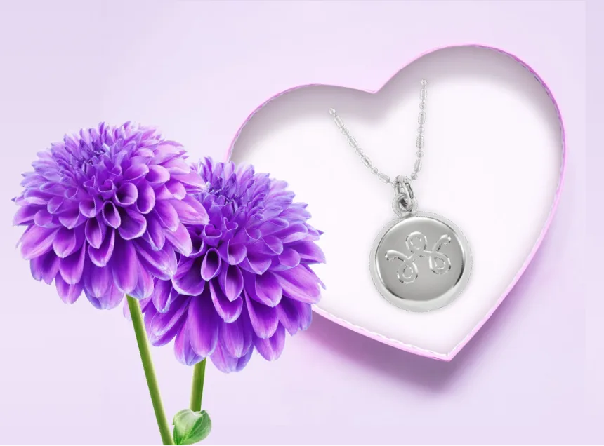 Un coffret en forme de cœur contenant un collier en argent avec un pendentif, à côté de dahlias violets, symbolise le précieux cadeau de la sécurité que les Accessoires de sécurité connectés offrent à vos proches.