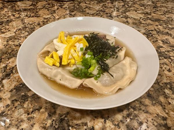 A bowl of rice cake mandu soup topped with egg, seaweed, and scallions.