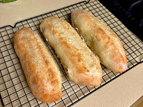 Loaves of crispy Italian bread cooling on a baking rack