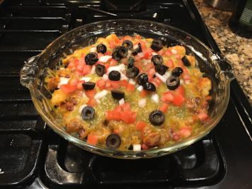 A dish of tater tot nachos with cheese, tomatoes, onions, and black olives.