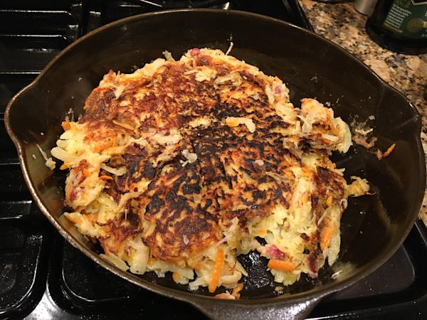A skillet with fried cabbage and shredded potato pie.