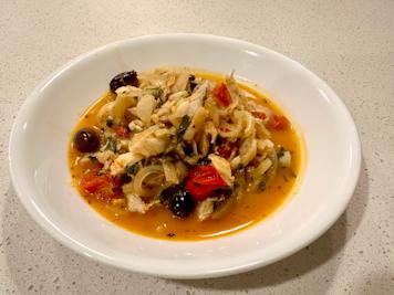A bowl of cod fish stew with onions, fennel, tomatoes, and black olives.