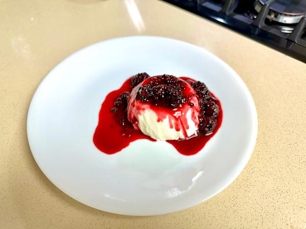 A ramekin of panna cotta with blackberry compote.