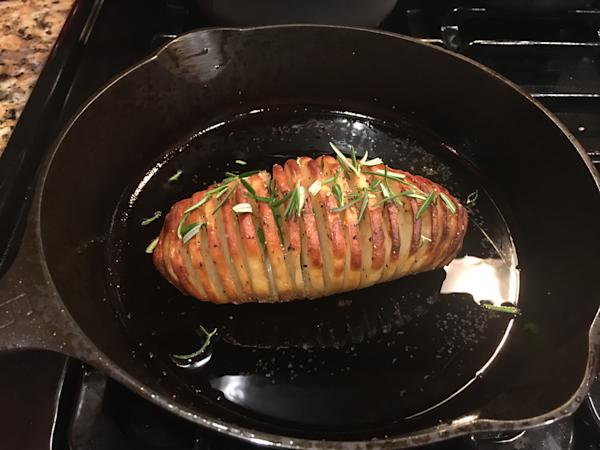 Roasted hasselback potato with garlic and rosemary in a cast iron skillet.