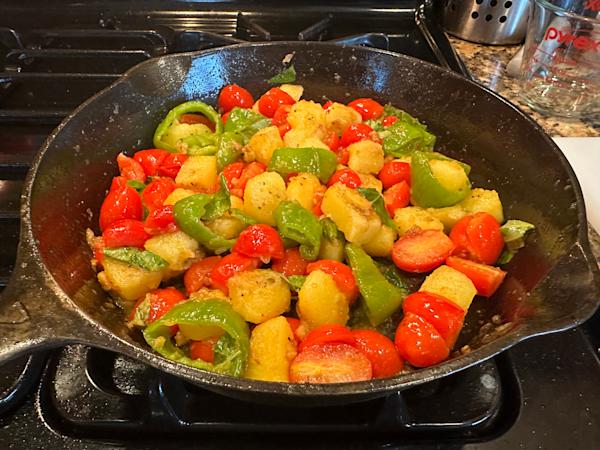 A skillet with fried potatoes, Iitalian frying peppers, and grape tomatoes.