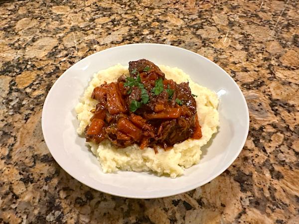 A plate of boeuf bourguignon over a bed of mashed potatoes.