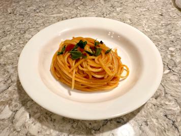 A plate of tomato water pasta topped with basil.