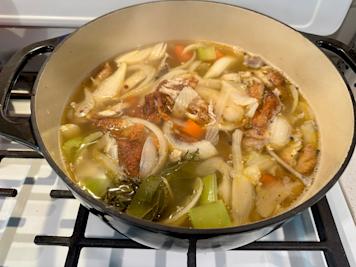 A pot of chicken stock simmering on a stove.