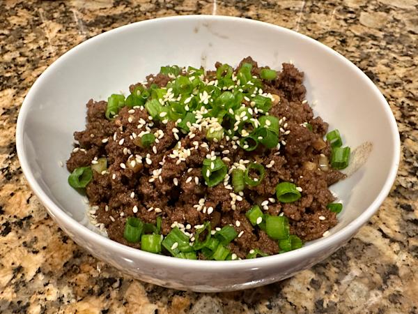 A bowl of bulgogi-style ground beef topped with scallions and sesame seeds.