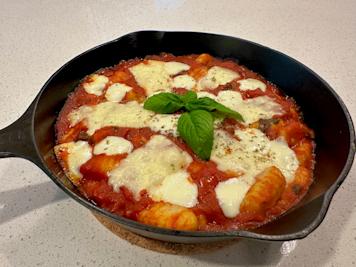 A skillet full of gnocchi alla sorrentina covered withe melted mozzarella cheese and basil.