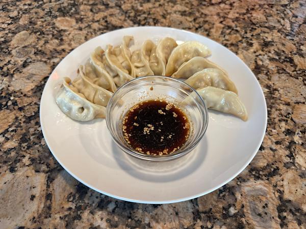 A plate of steamed dumplings with a dish of dipping sauce.
