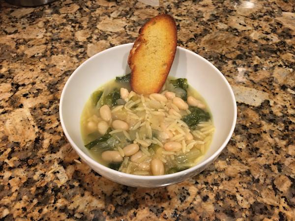 A bowl of escarole soup with white beans and orzo.