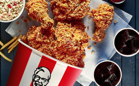 KFC chicken spills out of a KFC bucket on a table.