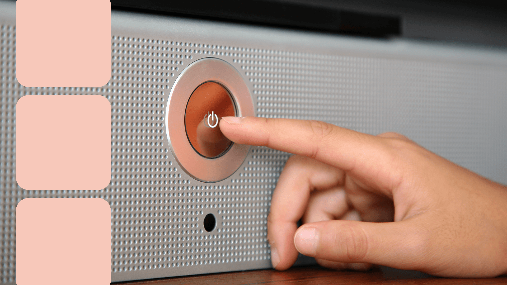 Finger pressing a circular power button on a metallic perforated surface, with the power symbol illuminated in orange