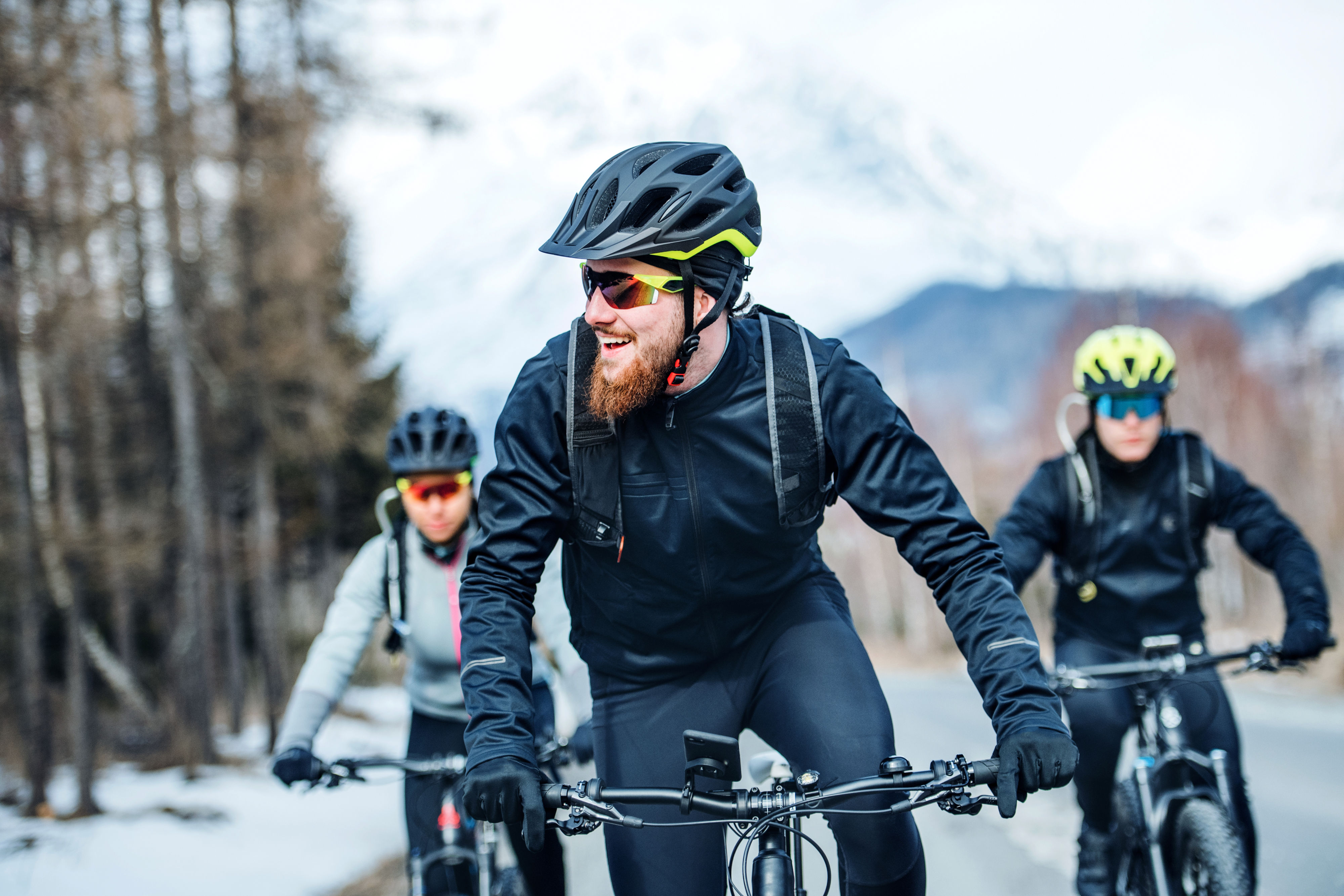 Drei sportliche Fahrradfahrer, die durch einen winterlichen Wald fahren.