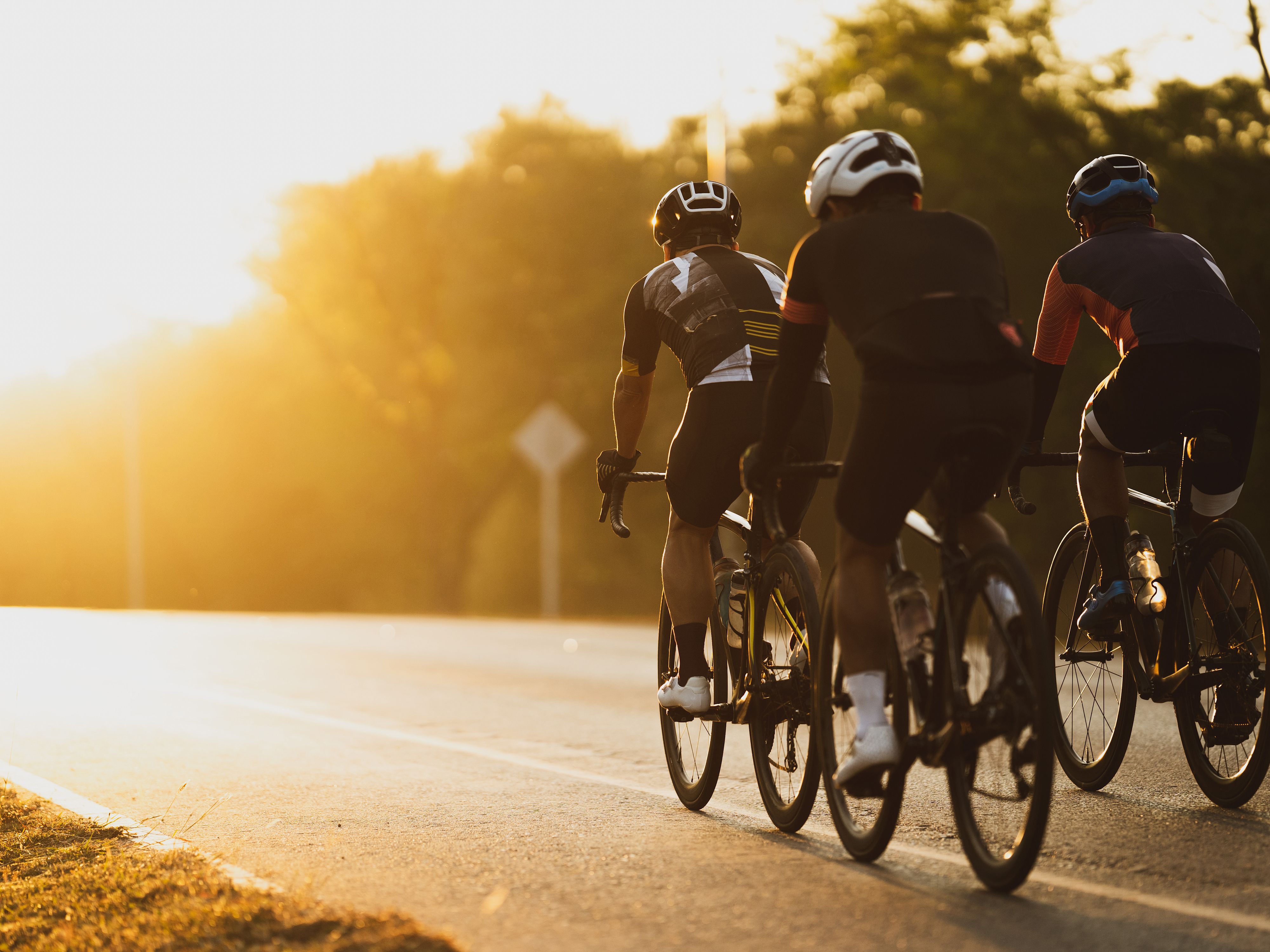 Gruppe von Rennrad Fahrern auf der Straße mit Sonnenuntergang im Hintergrund