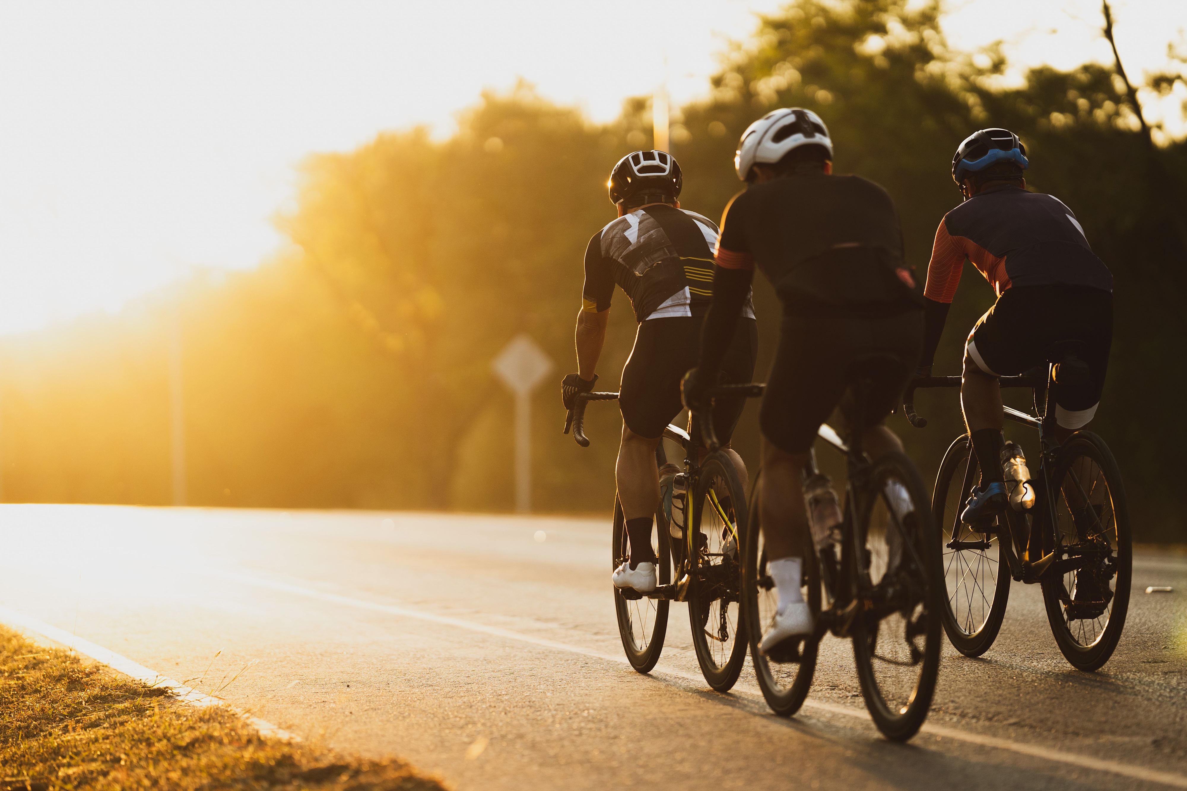 Gruppe von Rennrad Fahrern auf der Straße mit Sonnenuntergang im Hintergrund