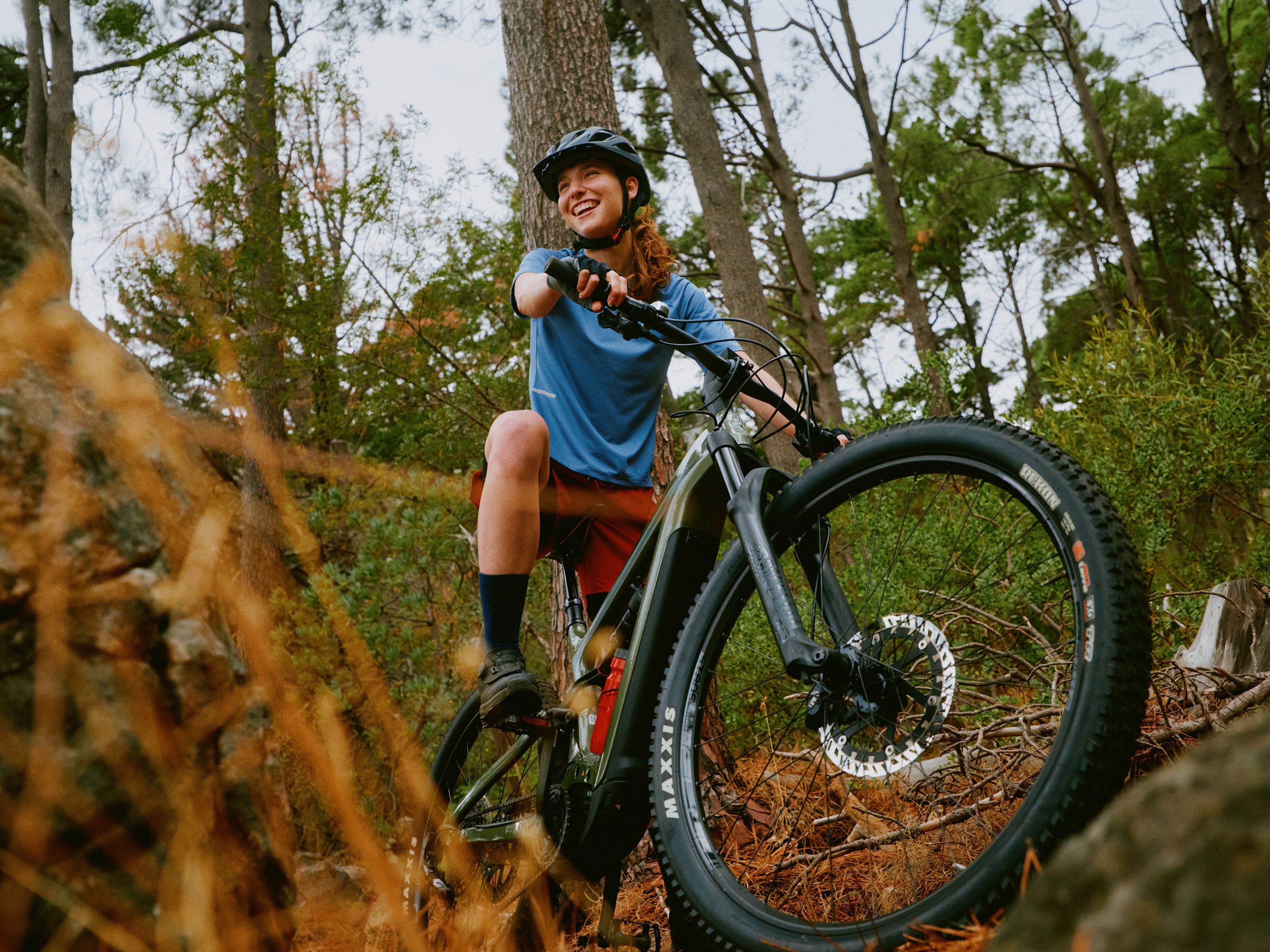Mountainbikerin mit rotem Helm klettert mit ihrem Bike über einem Baumstamm im Wald.