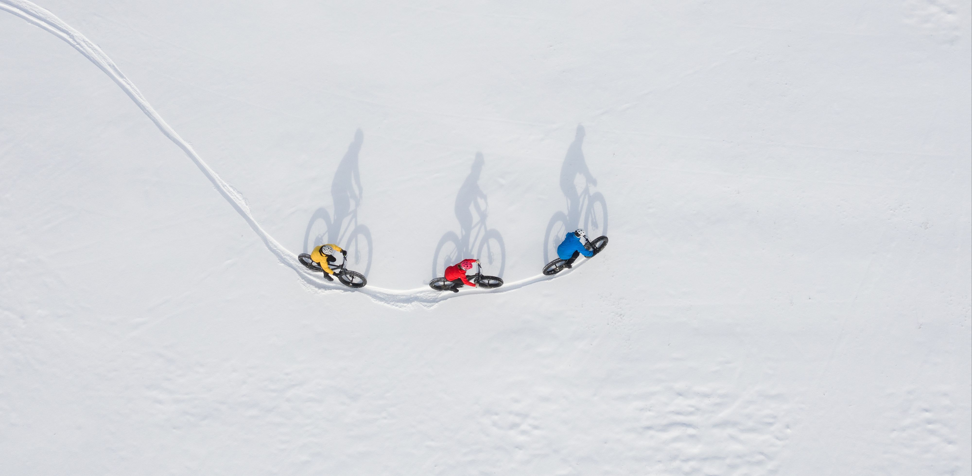 Drei farbenfroh gekleidete Fahrradfahrer, die hintereinander durch den Schnee fahren