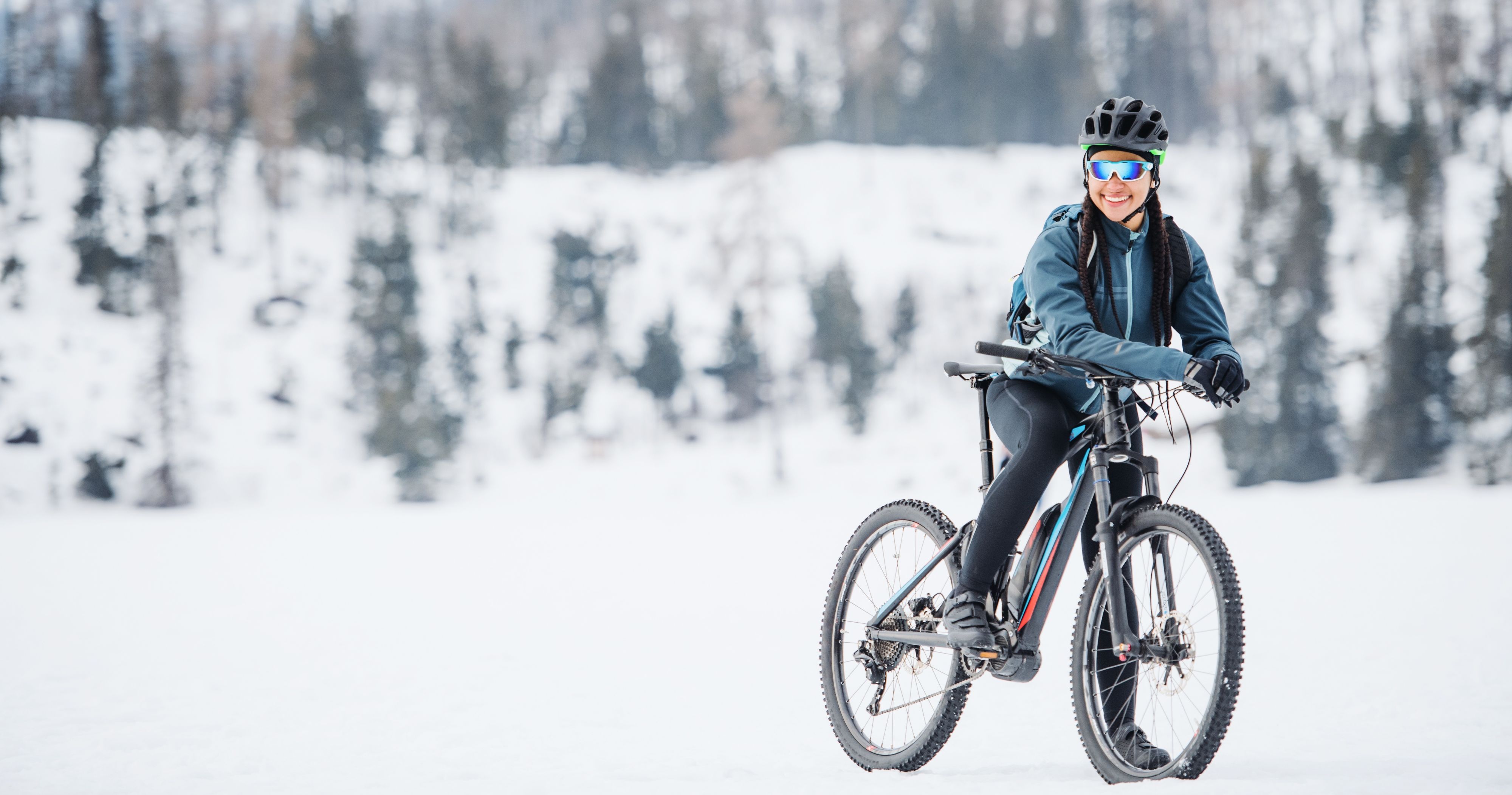 Sportlich gekleidete Frau auf einem Fahrrad, die durch einen winterlichen Wald fährt und den Ausblick genießt