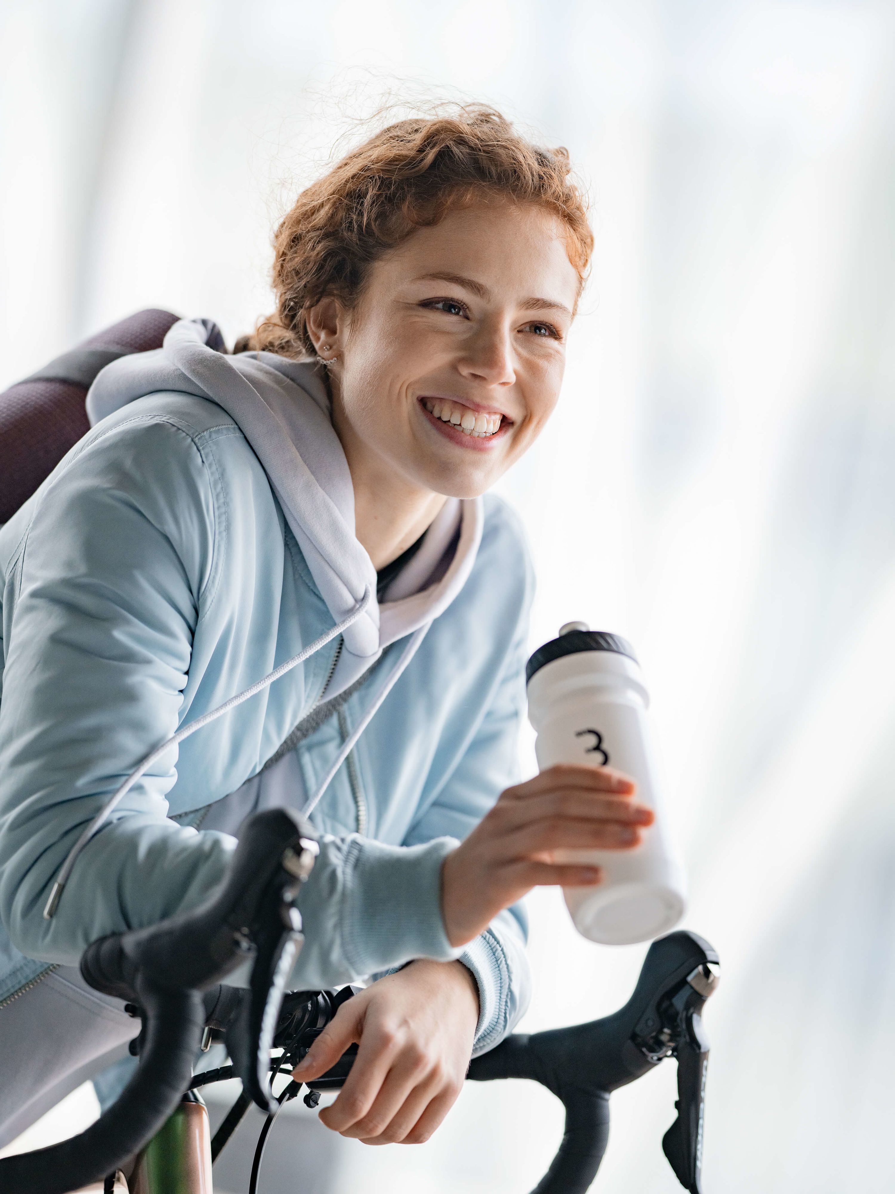 Frau, die sich auf Fahrrad lehnt mit Wasserflasche in der Hand