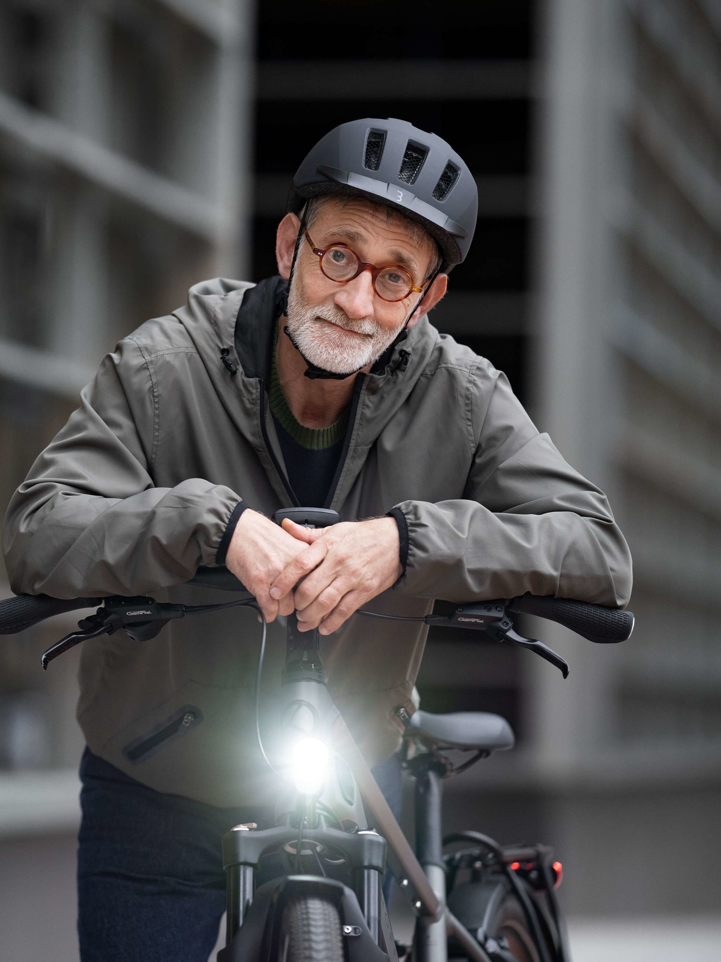 Lächelnder Mann mit grauem Bart und Fahrradhelm, der sich über seinen Lenker Richtung Kamera beugt.
