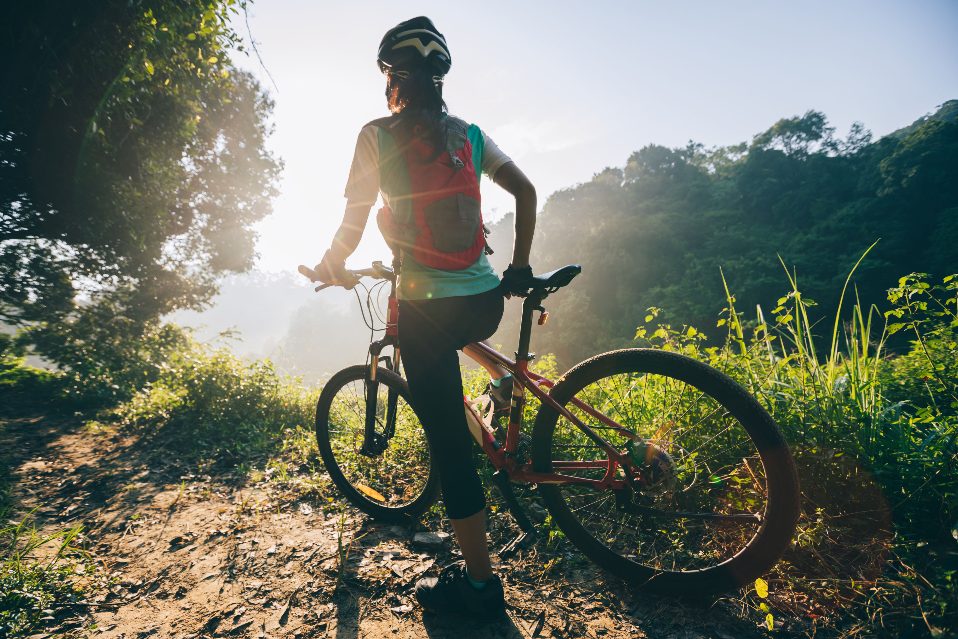 Sportlicher Fahrradfahrer der in der Natur steht und den Ausblick auf einen Wald bewundert.