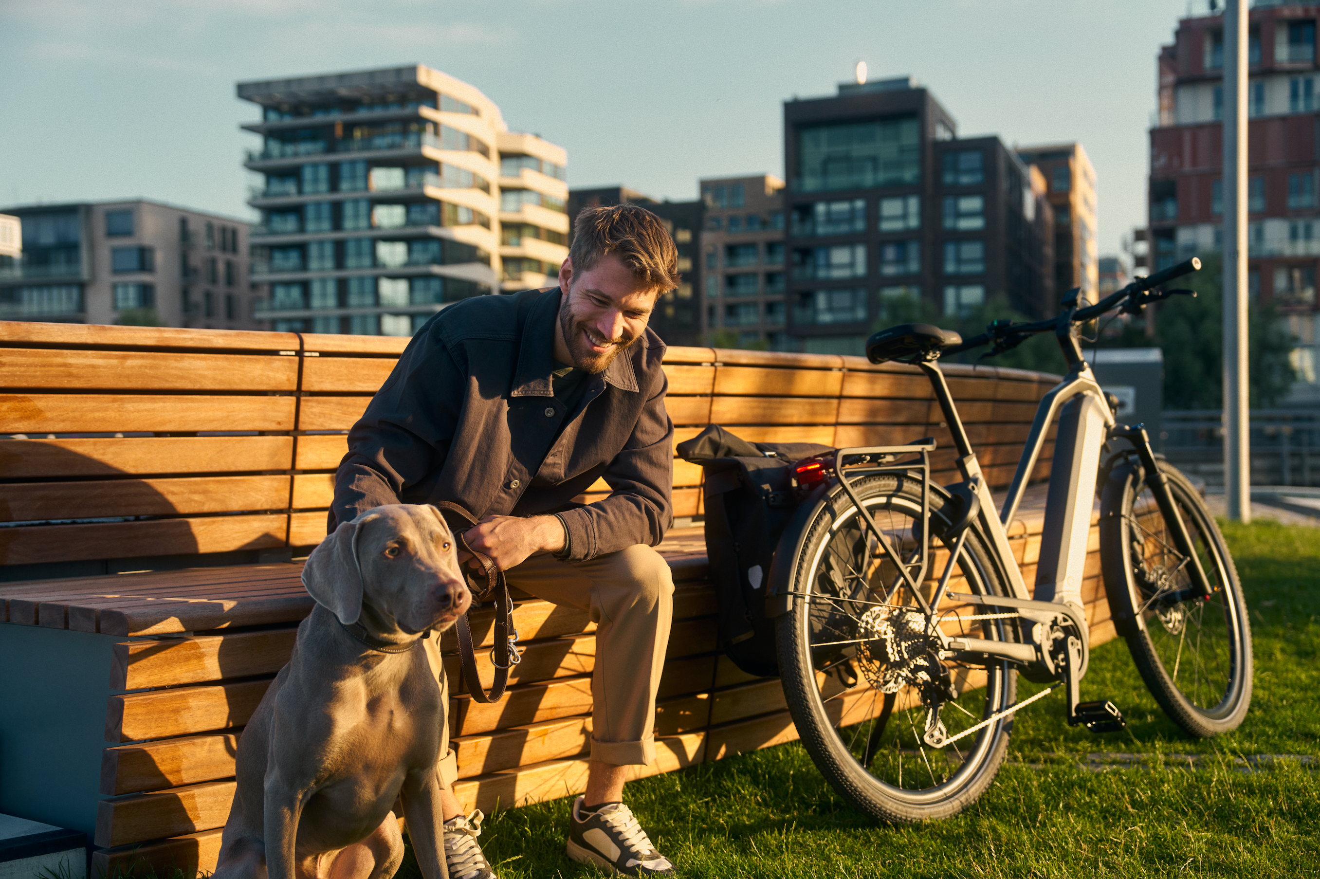 Mann der neben einem Fahrrad und einem Hund auf einer Bank sitz 