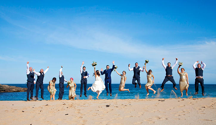 Wedding party jumping on beach after ceremony