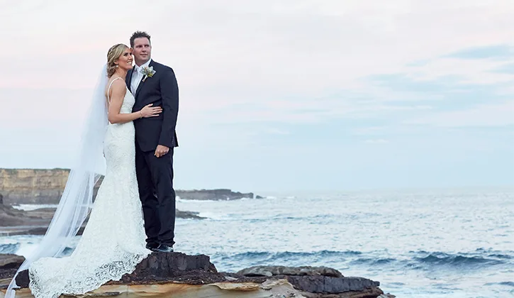 Bride and groom posing on the rocks by the ocean