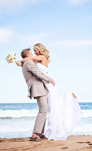 Husband lifting up wife on the beach after their wedding