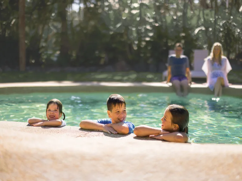 Three kids in resort pool, leaning on pool edge