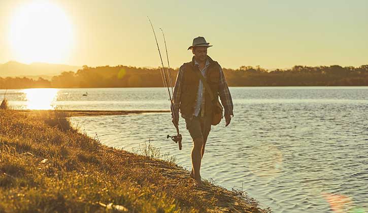 Person walking along the edge of water with a fishing rod